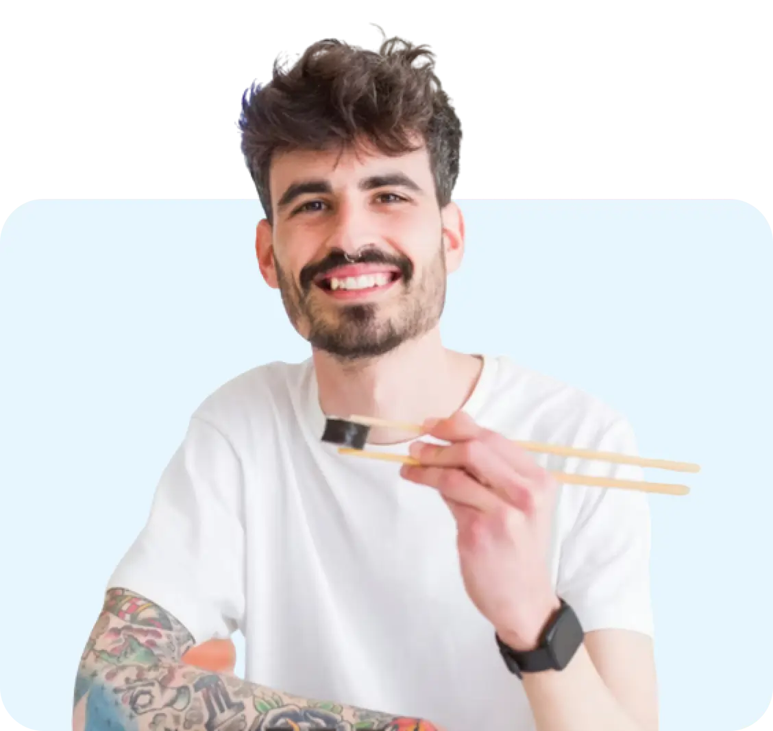 A young man smiling and eating sushi